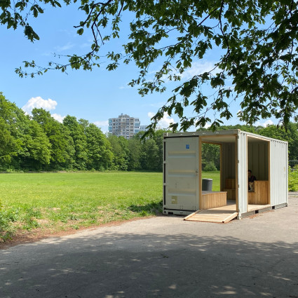 View across the meadow of the sports park to the city quarter "Südseite"; a container with seating invites you to linger.