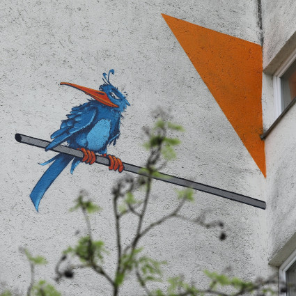 Auf der nächsten Hauswand sitzt ein blauer Vogel auf der Querflöte des Flötenspielers.