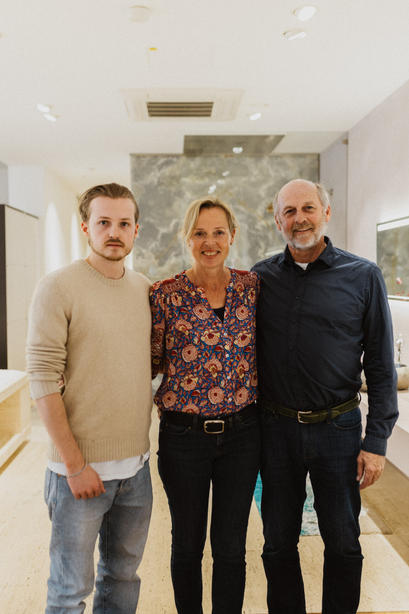 Auf diesem Foto sieht man einen Teil der Familie Obermaier. Ganz rechts außen ist der Inhaber Josef Obermaier zu sehen. Er trägt ein dunkles Hemd mit einer dunklen Hose und lächelt. In der Mitte steht seine Frau Marianne Obermaier, ebenfalls Inhaberin. Sie trägt eine gemusterte Bluse und dazu eine dunkle Hose. Links außen im Bild steht der Sohn des Ehepaars, Mika Obermaier. Er trägt einen brauen Pullover, darunter ein weißes Shirt und eine Jeans. Die Drei stehen im Verkaufsraum.