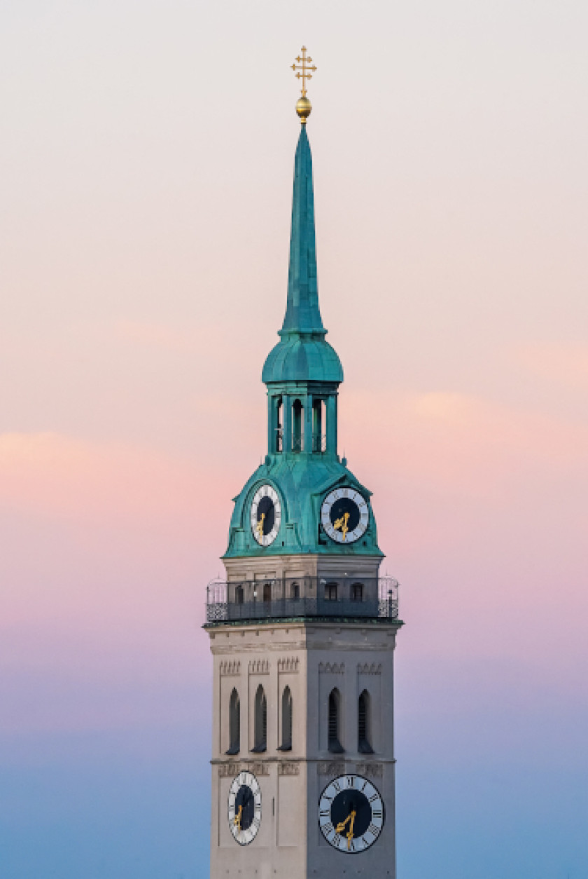 Auf diesem Bild ist ein Teil der oberen Hälfte des Turms der Sankt Peter Kirche in München vor dem Abendrot zu sehen. Der Turm ist mittig im Bild. Auf der Turmspitze sind zwei Uhren auf den zwei erkennbaren Seiten zu sehen. Das Dach ist grünlich-metallisch. Darunter ist eine Aussichtsplattform zu erkennen. Darunter auf dem Turm sind erneut zwei Uhren auf den zwei erkennbaren Seiten zu sehen. Ganz oben auf der Turmspitze ist ein goldenes Symbol.