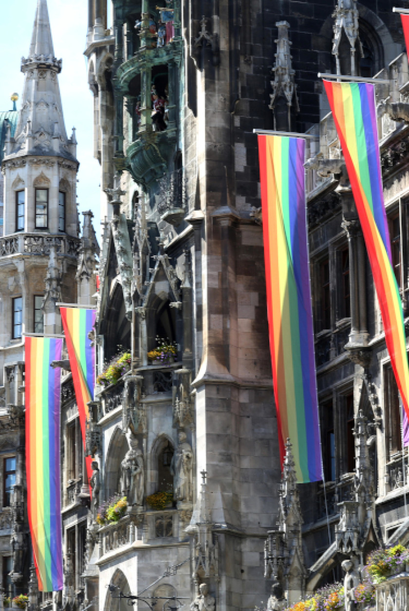 Auf diesem Foto sieht man vier bunte Fahnen, die von einem Gebäude hängen.