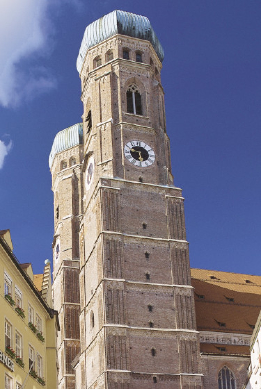 Auf diesem Foto sieht man zwei Türme aus Backsteinen von unten seitlich. Die Türme haben ein grünes Dach auf der Spitze und Uhren. Ein kleiner Teil des Kirchenschiffs ist hinter den Türmen noch erkennbar.